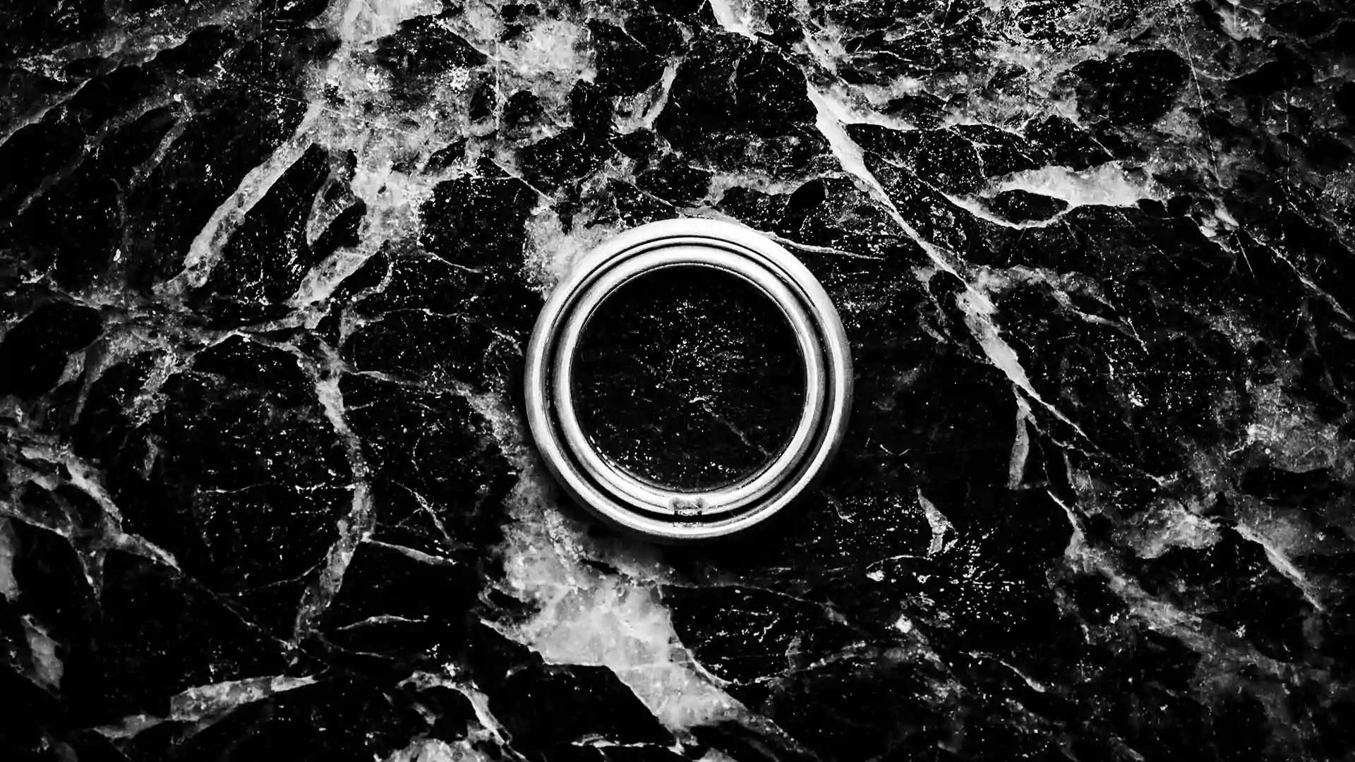 Detailaufnahme von Trauringen auf Marmor. Die Ringe passen perfekt ineinander. Schwarz-Weiß